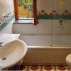 Bagno con vasca, lavandino, WC e finestra. Piastrelle bianche e dettagli decorativi.