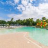 Una piscina con scivolo colorato e aree prendisole, alberi intorno e cielo nuvoloso.