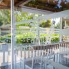 Tavoli e sedie in un lounge con pareti di vetro, vista esterna sul verde.