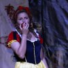 Persona in costume da Biancaneve con una mela in mano, sfondo teatrale.