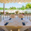 Tavolo apparecchiato su terrazza con vista su piscina e fiori colorati attorno.