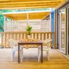Terrazza in legno con tavolo da pranzo, sedie bianche e decorazioni floreali.