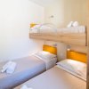 Camera con due letti singoli e letto a castello, testiere arancioni e asciugamani piegati.