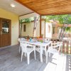 Veranda con tavolo bianco, sedie e recinzione in legno, circondata da alberi.