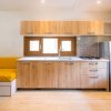 Cucina moderna con mobili in legno chiaro, frigorifero e panca con cuscini gialli.