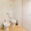Bagno con bidet, water, scovolino e porta bianca chiusa, pavimento in legno chiaro.