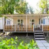 Casa mobile con veranda, staccionata in legno, tavoli e sedie, circondata da alberi.