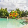 Piscina con scivoli colorati al centro, circondata da alberi e panchine.