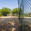 Campo sportivo con porta da calcio e recinzione, ombreggiato da alberi.