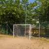 Un campo da calcio con una porta e una rete metallica, circondato da alberi.