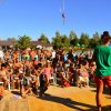 Festa all'aperto con molte persone sedute, intorno a una piscina e palme.