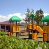 Area giochi all'aperto con strutture gialle e tetti verdi, circondata da vegetazione.