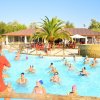 Lezione di acquagym in una piscina all'aperto con partecipanti e istruttrice in divisa rossa.