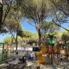 Parco giochi all'aperto con scivolo giallo e tavoli da pic-nic, circondato da alberi alti.