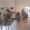 Una palestra con tapis roulant, cyclette e attrezzi vari, pavimento in legno chiaro.