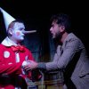 Un uomo si esibisce con un costume da clown con lungo naso mentre parla con un altro uomo.