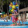 Persone in piscina accanto a una colorata statua di fiore sorridente.