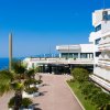 Edificio moderno di un hotel, vista sul mare con palme e cielo blu.