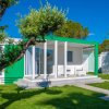 Bungalow moderno bianco e verde circondato da prato e alberi.