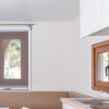 Interno di una cucina con finestre marroni, mobile bianco e lavello in acciaio.