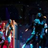 Persone che ballano su un palco illuminato da luci blu e stelle proiettate.