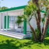 Una villetta bianca e verde con veranda, circondata da erba e alberi tropicali.