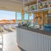 Un bar moderno con vista sulla spiaggia, ombrelloni arancioni fuori.