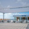 Un'ampia terrazza con sedie e tavoli bianchi e neri, ombrelloni arancioni sullo sfondo.