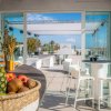 Sala con tavoli bianchi e panche, vista esterna mare. Frutta fresca in primo piano.