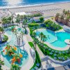 Complesso di piscine vicino a una spiaggia, con palme e giochi d'acqua colorati.