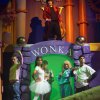 Scena teatrale con personaggi davanti a un ingresso Wonka colorato.