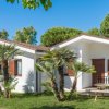 Bungalow bianchi con persiane marroni circondati da alberi e palme sotto un cielo blu.