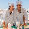 Due chef sorridenti impastano su un tavolo esterno, indossando cappelli da cuoco.
