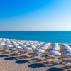 Spiaggia con file ordinate di ombrelloni bianchi e il mare azzurro sullo sfondo.