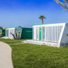 Case modulari bianche e verdi su prato verde con palme e cielo blu.