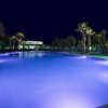 Piscina illuminata di viola con palme circostanti di notte.
