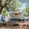 Camper parcheggiato tra alberi con sedie e tavolo fuori.