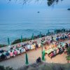 Cena all'aperto accanto al mare, con tavoli pieni di persone e ombrelloni verdi.