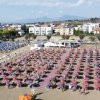 Spiaggia con file ordinate di ombrelloni colorati e lettini, affiancata da palazzi e vegetazione.