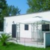Piccola casa bianca con gazebo su prato verde.