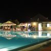 Piscina illuminata di notte con accanto un bar e persone sedute.