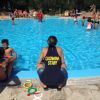 Piscina all'aperto con diverse persone. Figura con maglia 