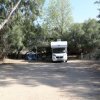 Un camper parcheggiato in un'area boschiva con un tendalino e sedie all'aperto.
