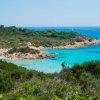 Una spiaggia con acqua turchese, circondata da colline verdi e rocce.