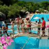 Persone su un ponte sopra una piscina con scivoli, circondata da fiori e verde.