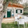 Tavolo bianco con sedie davanti a una casa immersa nel verde.