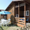 Una casetta di legno con veranda, tavolo e sedie bianche all'aperto sotto un grande ombrellone blu.