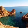 Scogliere rosse circondano acqua cristallina, con rocce emergenti nel mare aperto.