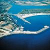 Veduta aerea di una costa con un porto e un lungomare, circondati da natura e corsi d'acqua.