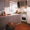 Cucina moderna con mobili grigi e elettrodomestici bianchi, parquet a terra.